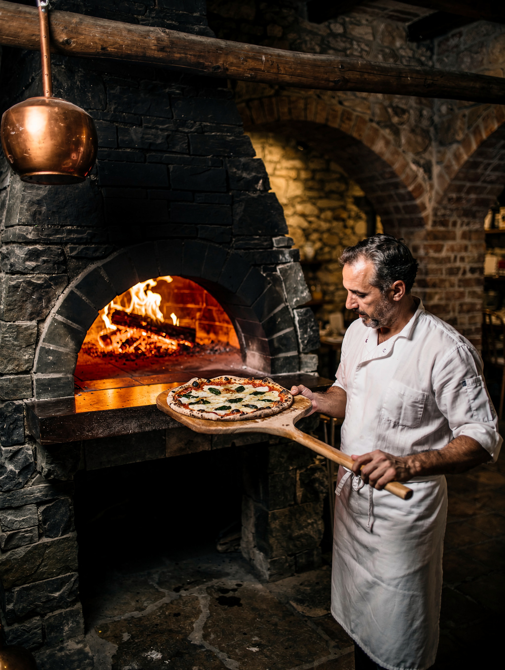 Chef firing handmade pizzas in the glowing brick hearth oven